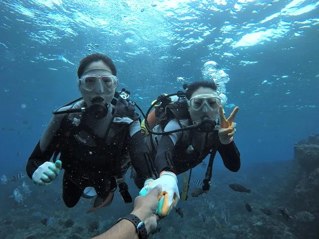 Two scuba divers underwater making a peace sign and holding hands