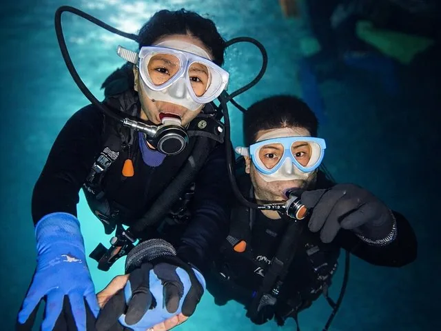 Man snorkeling underwater pointing at the camera among various fish